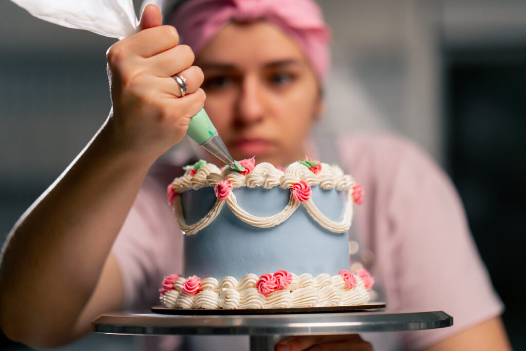 close up of a female baker in a professional kitchen decorating a blue cake with cream